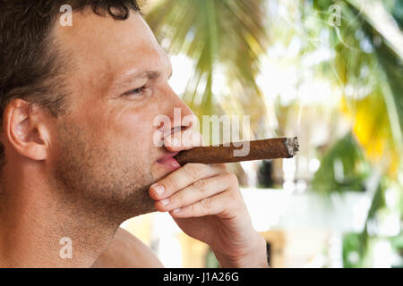 Young European man smokes big cigar, closeup profile portrait with selective focus. Dominican Republic Stock Photo