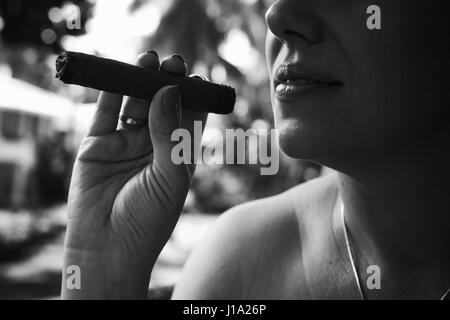 Young European woman smokes handmade cigar, closeup monochrome photo with selective focus. Dominican Republic Stock Photo