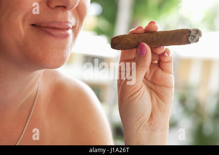 Young smiling European woman smokes handmade cigar, closeup photo with selective focus. Dominican Republic Stock Photo