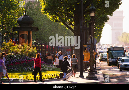 People walking on pavement by flower garden. Stock Photo