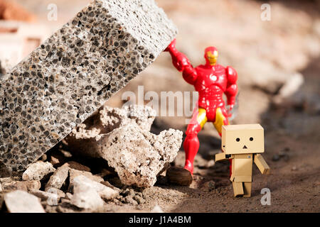 A Danbo Danboard character running away from falling masonary which is being held in place by a toy Iro Man character Stock Photo