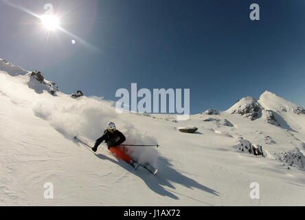 A skier makes a turn in powder snow with the sun hanging low on the sky. Stock Photo