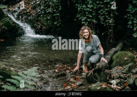 Caucasian woman crouching on rock in forest stream Stock Photo
