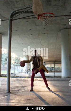 Black man wearing backpack playing basketball under overpass Stock Photo