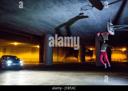 Headlights shining on Black man dunking basketball Stock Photo