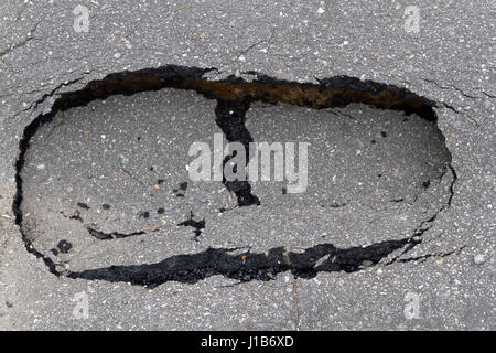 Close up of a small asphalt sinkhole in the road shaped like a big footprint Stock Photo