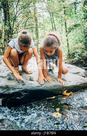 Mixed Race girls kneeling on rock looking at stream Stock Photo