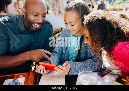 Father ad daughters texting on cell phone at restaurant Stock Photo