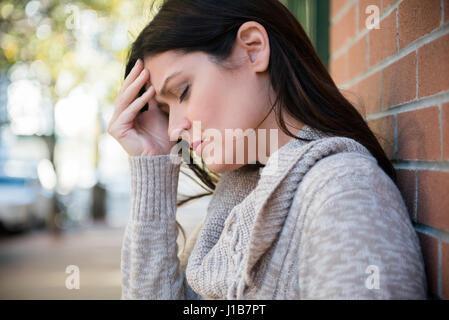 Caucasian woman with headache leaning on brick wall Stock Photo