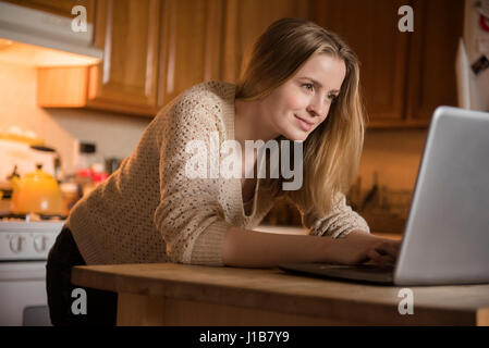 Smiling woman using laptop in domestic kitchen Stock Photo