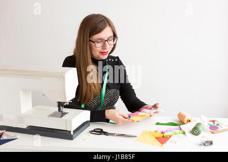 needlework and hand quilting in the workshop of a young woman, a tailor on white background - young smiling woman tailor holds in her hands sewn on the sewing machine the pieces of colorful fabrics Stock Photo