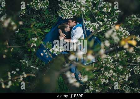Caucasian couple laying in grass under flowering trees Stock Photo
