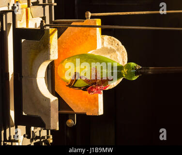 Glass making artists work on adding decoration to ornate green glass bottle or bowl Stock Photo