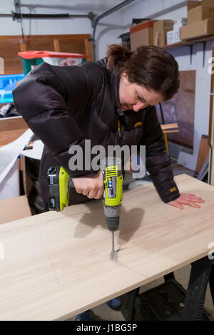 SPRINGFIELD, OR - JANUARY 31, 2017: Female construction worker using a driver to drill a hole through a wood vanity top on a major DIY house renovatio Stock Photo