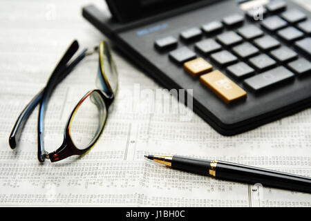 Calculator and glasses and pen on top of financial newspaper Stock Photo