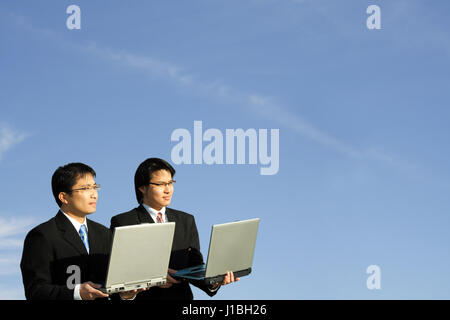 Two businessmen carrying their laptops outdoor on a sunny day Stock Photo