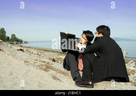 Two businessmen working on their laptop at the beach Stock Photo