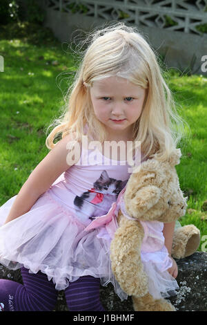 Little blonde girl, child holding her teddy bear dressed in matching tutus shy toddler concept, grumpy summer days blonde little girl curly Stock Photo