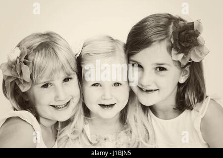 Portrait of three blonde girls sisters children family smliing with with flowers in their hair best friend concept, black white besties Stock Photo