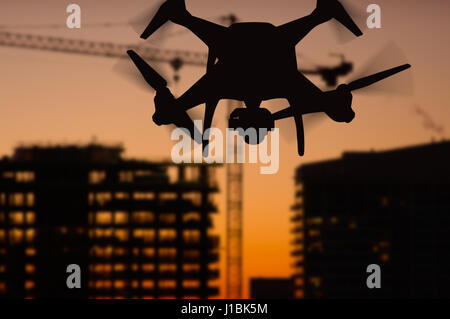Silhouette of Unmanned Aircraft System (UAV) Quadcopter Drone In The Air Over Buildings Under Construction. Stock Photo