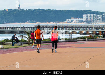 DURBAN, SOUTH AFRICA - APRIL 18, 2017: Many unknown people on paved beachfront promenade against piers and the Bluff in Durban, South Africa Stock Photo