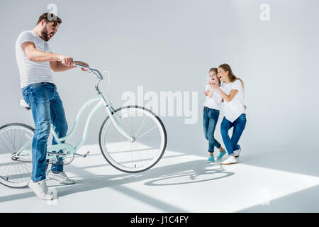 Laughing mother and daughter looking at emotional man having fun with bicycle Stock Photo