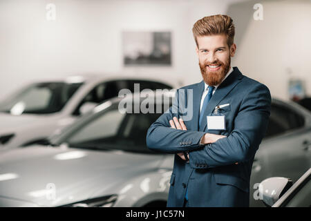 salesman in suit with crossed arms posing and looking at camera in dealership salon Stock Photo