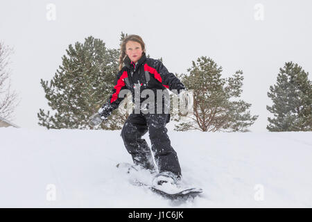 Serious girl riding snowboard on hill in winter Stock Photo