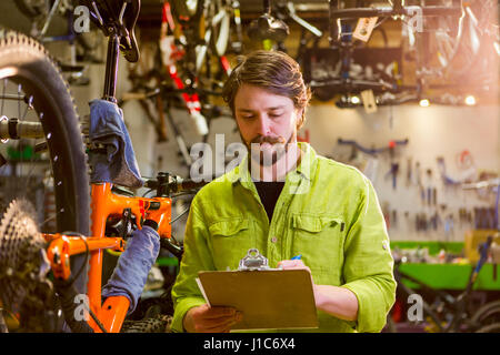 Caucasian worker writing on clipboard in bicycle shop Stock Photo