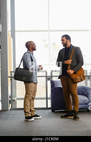 Men carrying briefcases talking in lobby Stock Photo