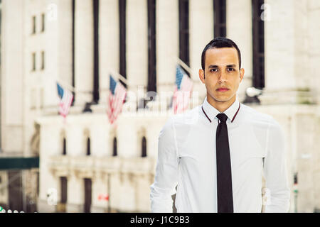 Young American Businessman wearing white shirt, black tie, standing outside vintage office building with USA flags on street, confidently looking forw Stock Photo