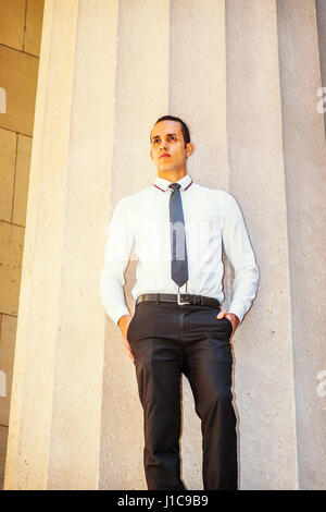 Young American Businessman wearing white shirt, black tie, hands in pockets, standing outside office building in New York, thinking, lost in thought. Stock Photo