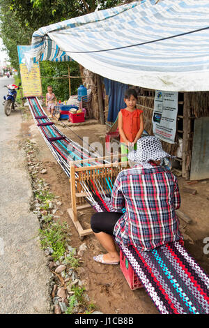 Woman working at loom, weaving extended rug  (18 meters) to be sectioned into smaller lengths, young daughter & son communicating with mother. Stock Photo