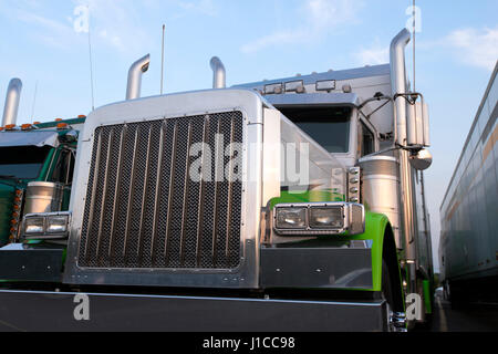 Big rig semi truck of classic American style with large chrome parts and a trailer in a row with another semi trucks and trailers on the truck stop. Stock Photo