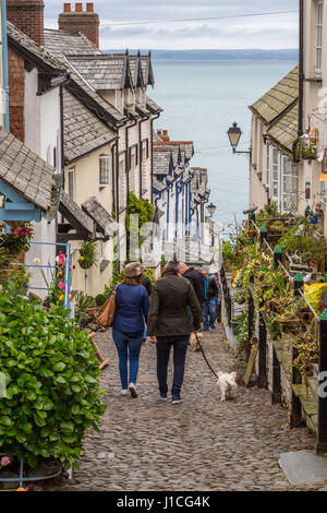 Clovelly, North Devon,England,UK. A couple walking a dog enjoy the  picturesque cottages, and steep cobbled high street of this secluded Devon village Stock Photo
