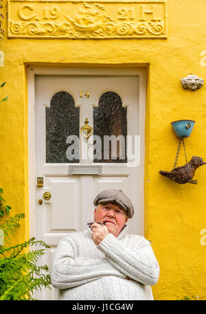 Clovelly,Devon,England, A resident of this picturesque village in North Devon enjoys sitting outside his brightly painted cottage smoking his pipe.UK Stock Photo