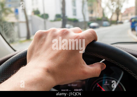 Steerind wheel with driver hand on it in modern car interior with view of street Stock Photo