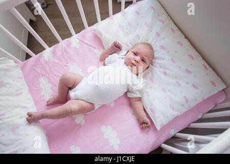 Two week old baby girl sleeping in her crib on pink sheets with cloud pattern.