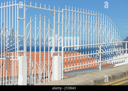 Decorative fence of forged metal painted white in bright sunlight on tiled roof and blue sky and sea background on upper street in Los Gigantes on Ten Stock Photo