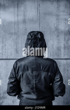Unrecognizable hooded female person facing concrete wall as ...