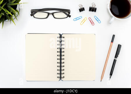 Open spiral blank notebook with pen, pencil, eye glasses, cup of coffee and small flower plant on white desk table, flat lay top view Stock Photo