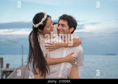 Young love Couple smiling under blue sky on wooden bridge near the sea Stock Photo