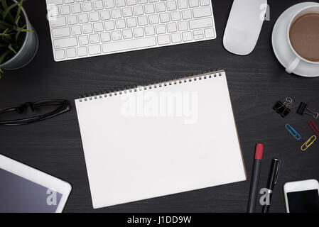Modern black office desk table with computer, tablet, cellphone, other supplies, eye glasses, cup of coffee and blank notebook page for input the text Stock Photo