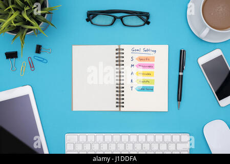 Smart goal setting on notebook with office supplies, computer, eye glasses and coffee cup over blue desk background, Business success concept Stock Photo