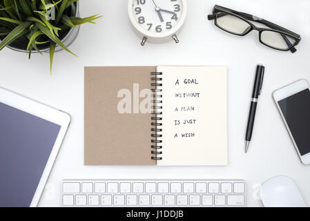 Goal without a plan is just a wish, quote business in open notebook with pen, eye glasses, smart phone, tableb, keyboard, mouse, alarm clock and small Stock Photo