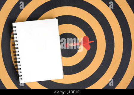 Arrow hitting in bullseye target on dartboard with open spiral notebook Stock Photo