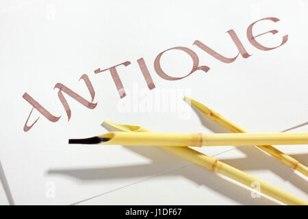 Word antique written with brown ink on the white paper sheet and three reed pens (calamus, qalam) beside Stock Photo