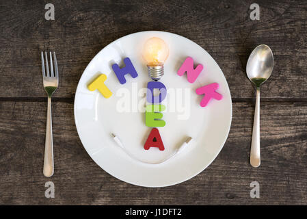 Creative thinking and smart idea concept, Bright light bulb with think and idea in plate with spoon and fork on grunge table background Stock Photo
