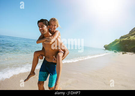 Portrait of loving couple piggyback together on tropical beach. Man carrying girlfriend on his back along the sea shore. Enjoying summer vacation. Stock Photo