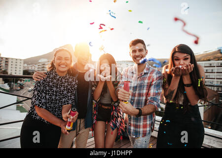 Group of friends hanging out together and blowing confetti on rooftop party. Stock Photo